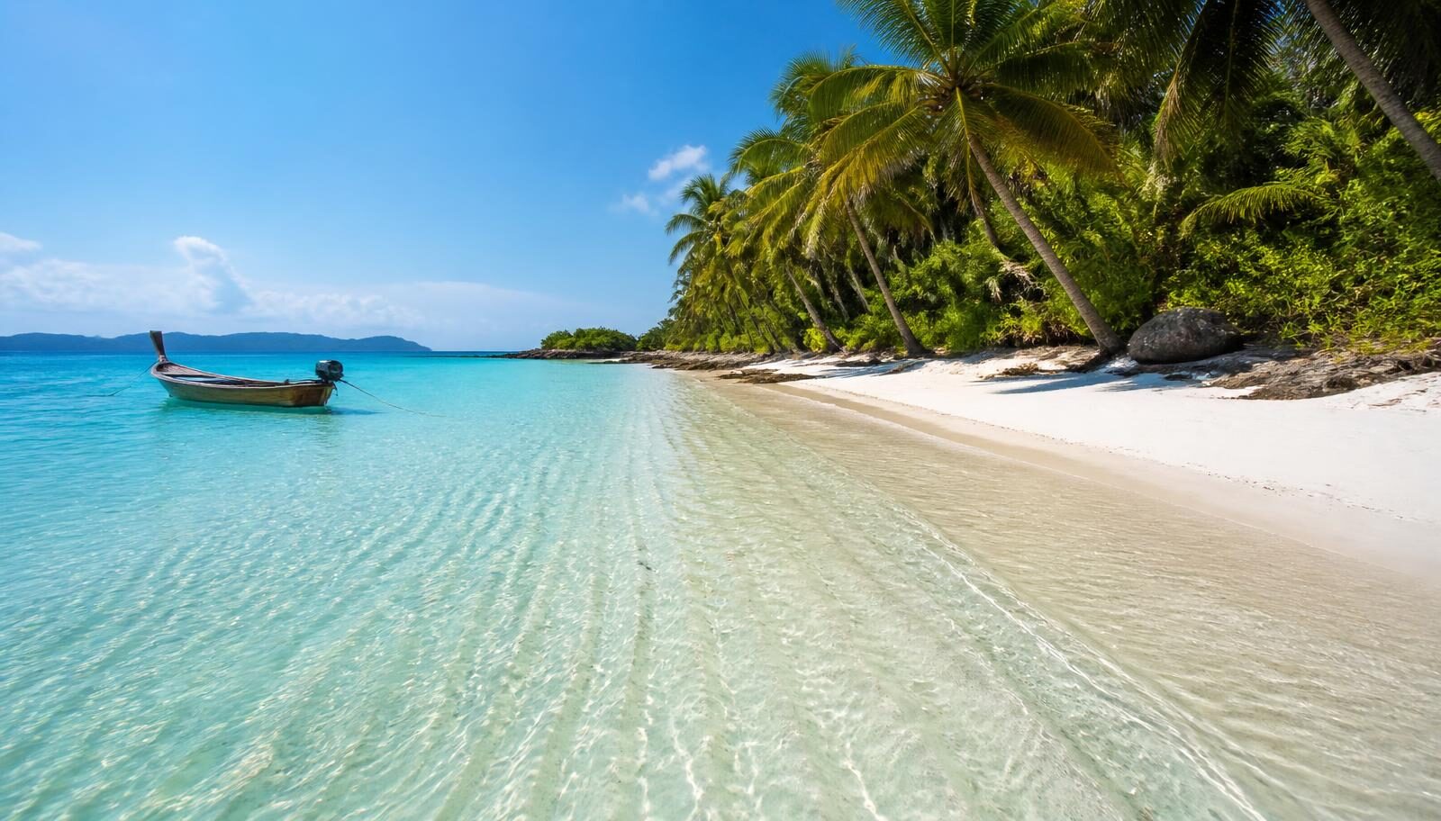 Clear turquoise shallows over pale sand beside a palm-lined island shoreline