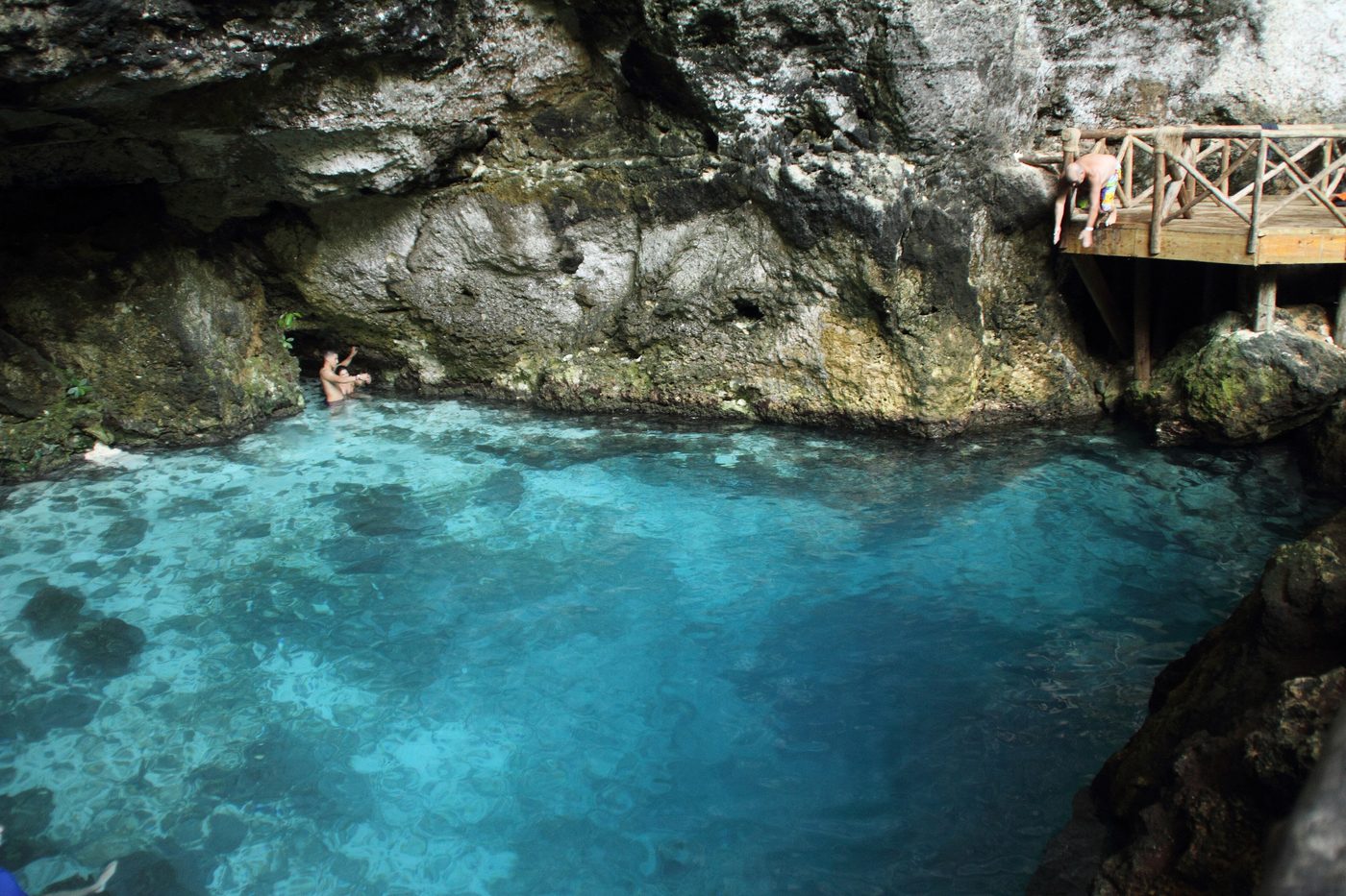 Swimmers in a turquoise cenote surrounded by limestone rock
