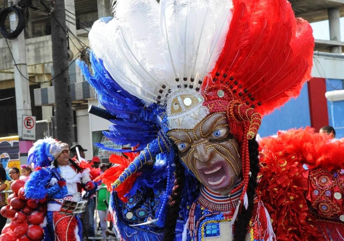 Costumed carnival dancer in an elaborate feathered Diablo Cojuelo mask at a Dominican street parade