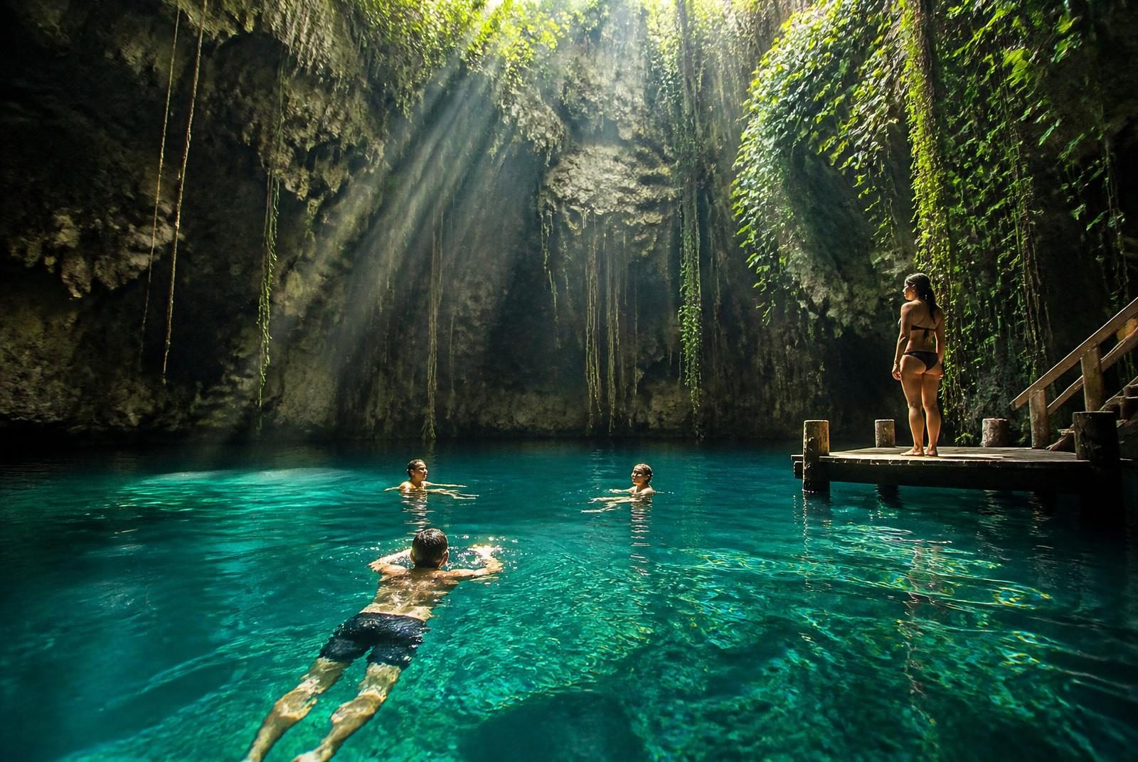 Cancun excursion in Mexico: adult travelers swimming in a jungle cenote near Cancun with sunlight beaming through the opening