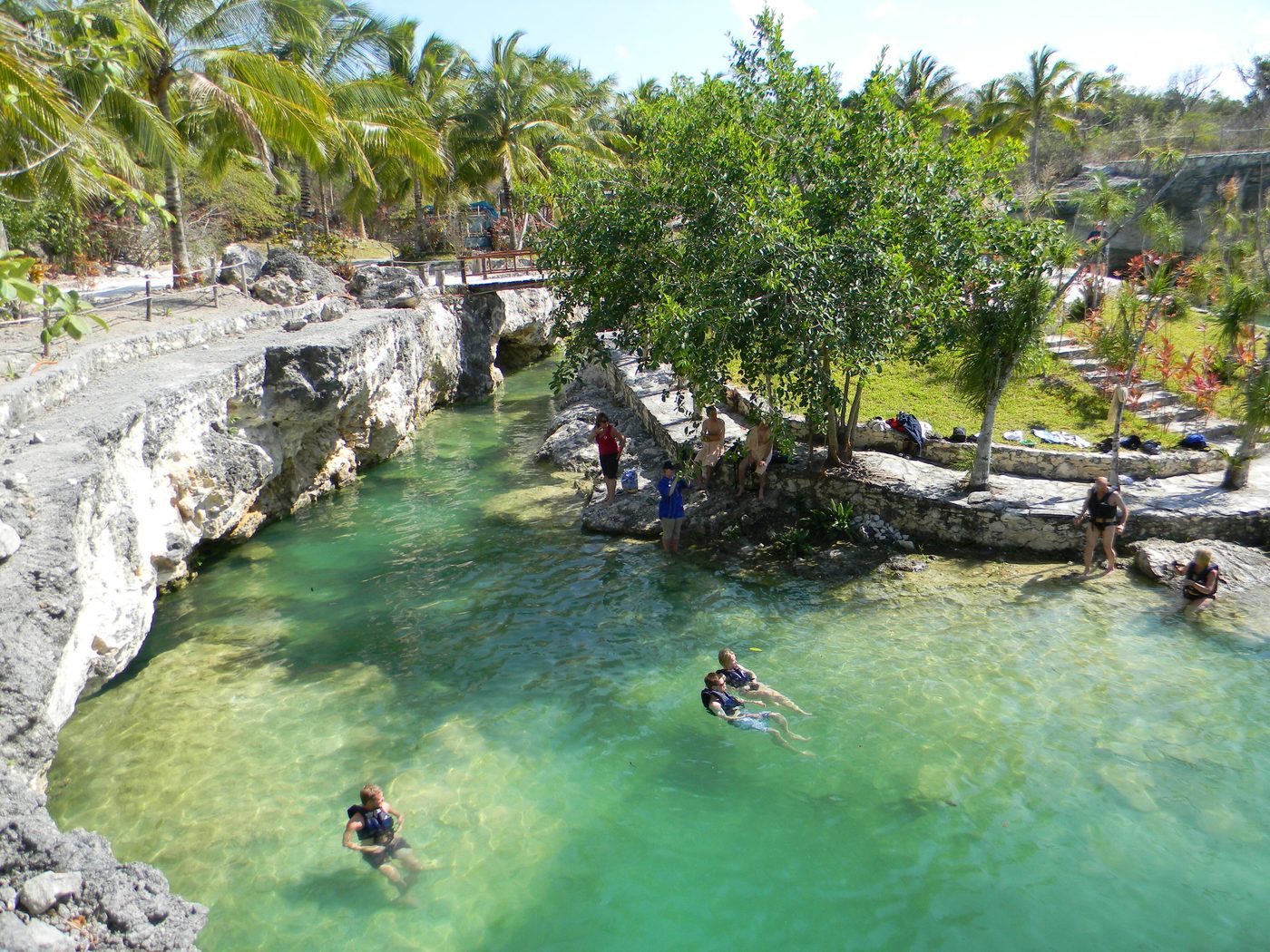 Bright blue limestone cenote pool surrounded by cliff walls and dense tropical vegetation