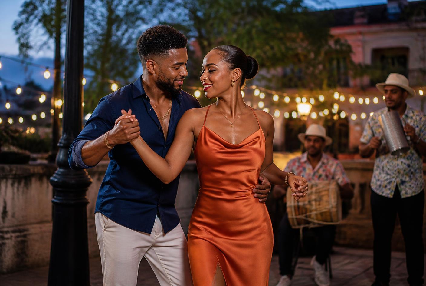 Couple dancing bachata under string lights while musicians play tambora and guira
